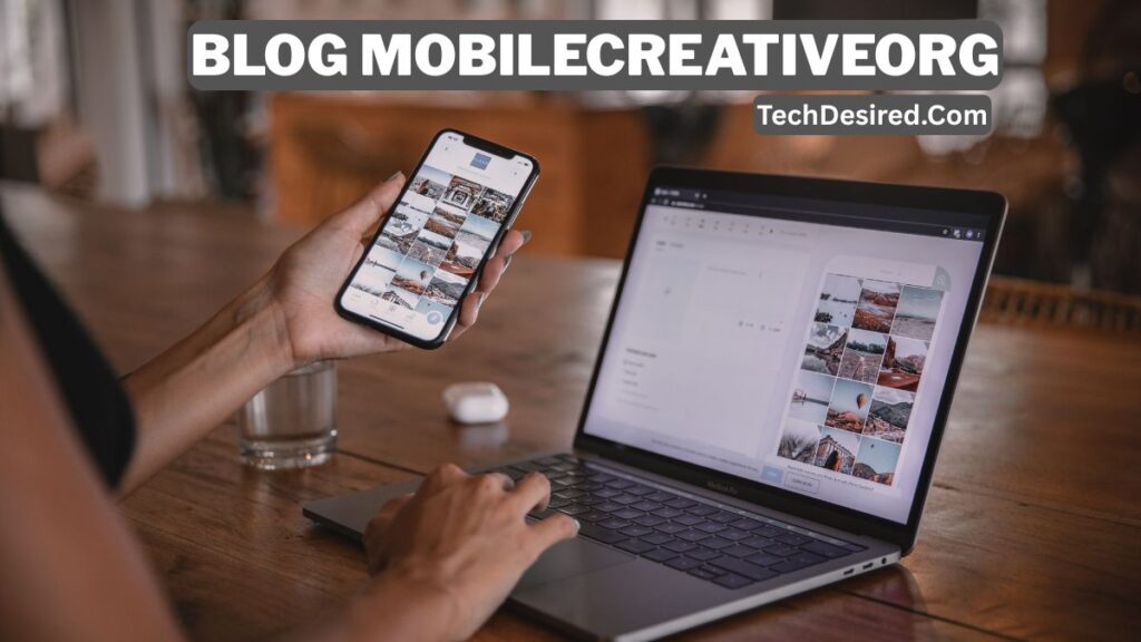 Person working on a laptop at a wooden desk while holding a smartphone, both screens displaying photo grids and content management tools, with text overlay reading “Blog MobileCreativeOrg – TechDesired.com.”
